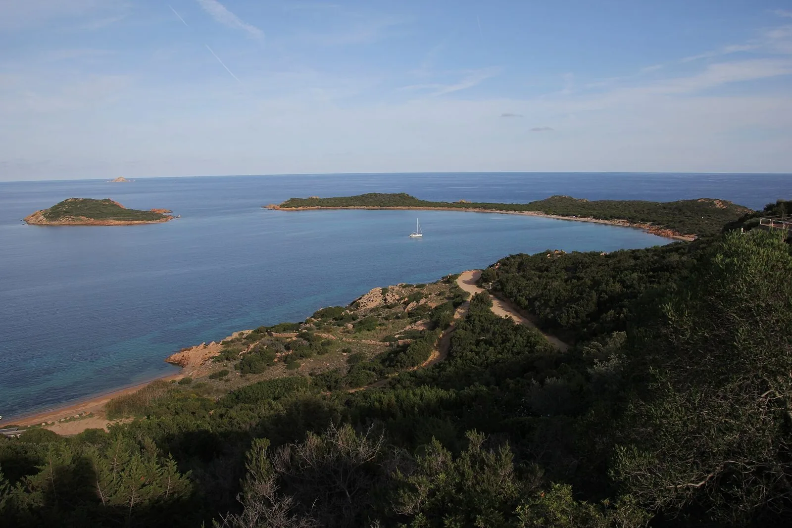 Capo Coda Cavallo dall'alto: macchia mediterranea, una spiaggia deserta, una barca a vela isolata nella baia e un isolotto al largo