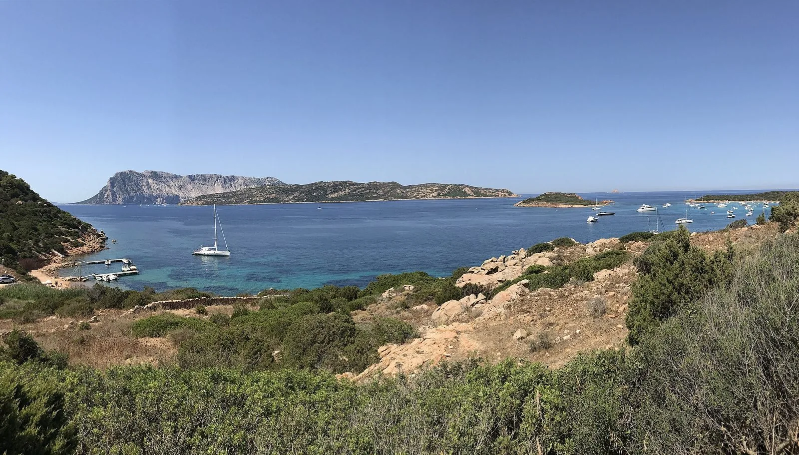 Panorama da Capo Coda Cavallo sul mare turchese con barche alla fonda, l'isola di Molara e il massiccio di Tavolara sullo sfondo